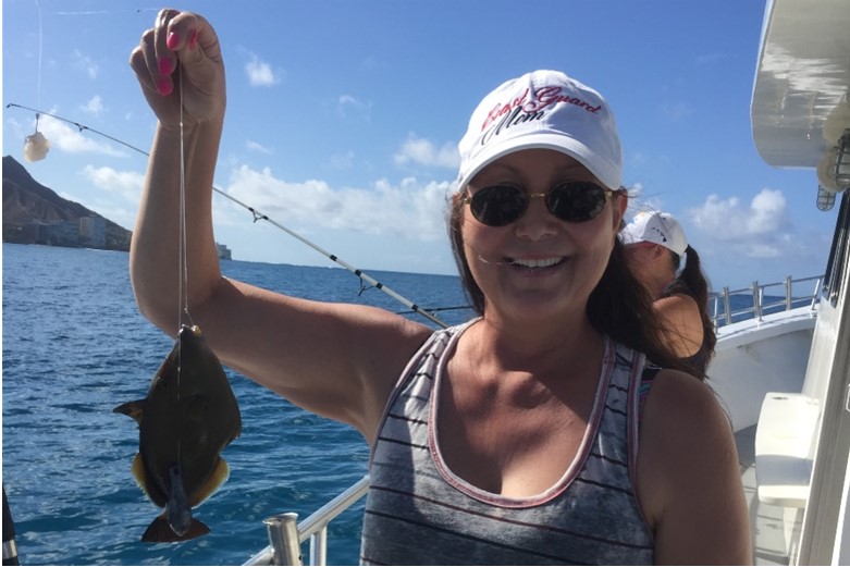 A woman holds up a fish while on a boat.