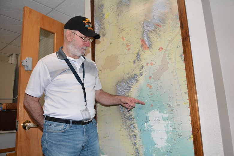 A man stands in front of a map pointing to a location