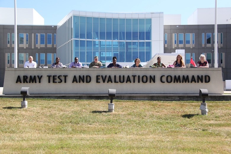 People stand behind a concrete sign that says Army Test and Evaluation Command outside of the headquarters building