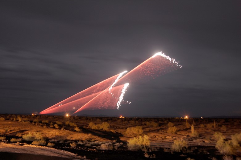 Field at night where ammunition is being fired and streaks can be seen in the sky