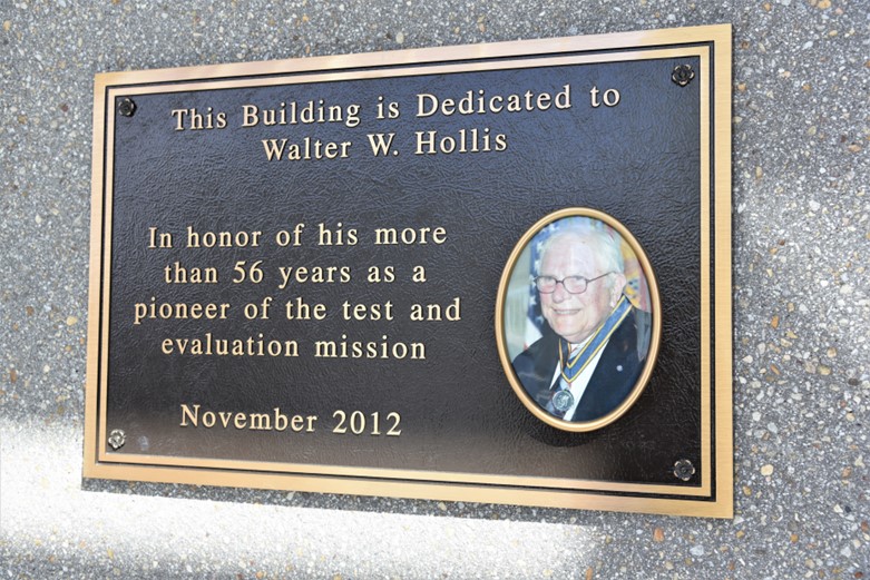 A plaque that reads "This Building is Dedicated to Walter W. Hollis. In honor of his more than 56 years as a pioneer of the test and evaluation mission. November 2012.