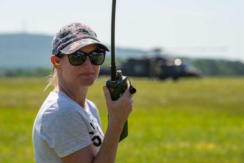 A woman holding a walkie talkie stands in front of a helicopter.