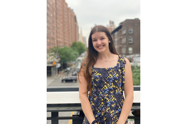 A girl in a dress is smiling with a city background.