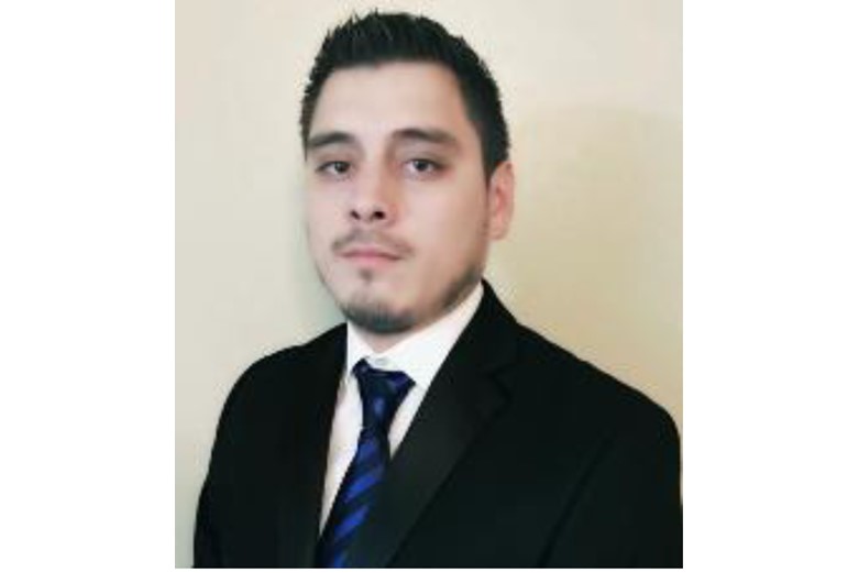 A man wearing a suit and tie in front of a beige background