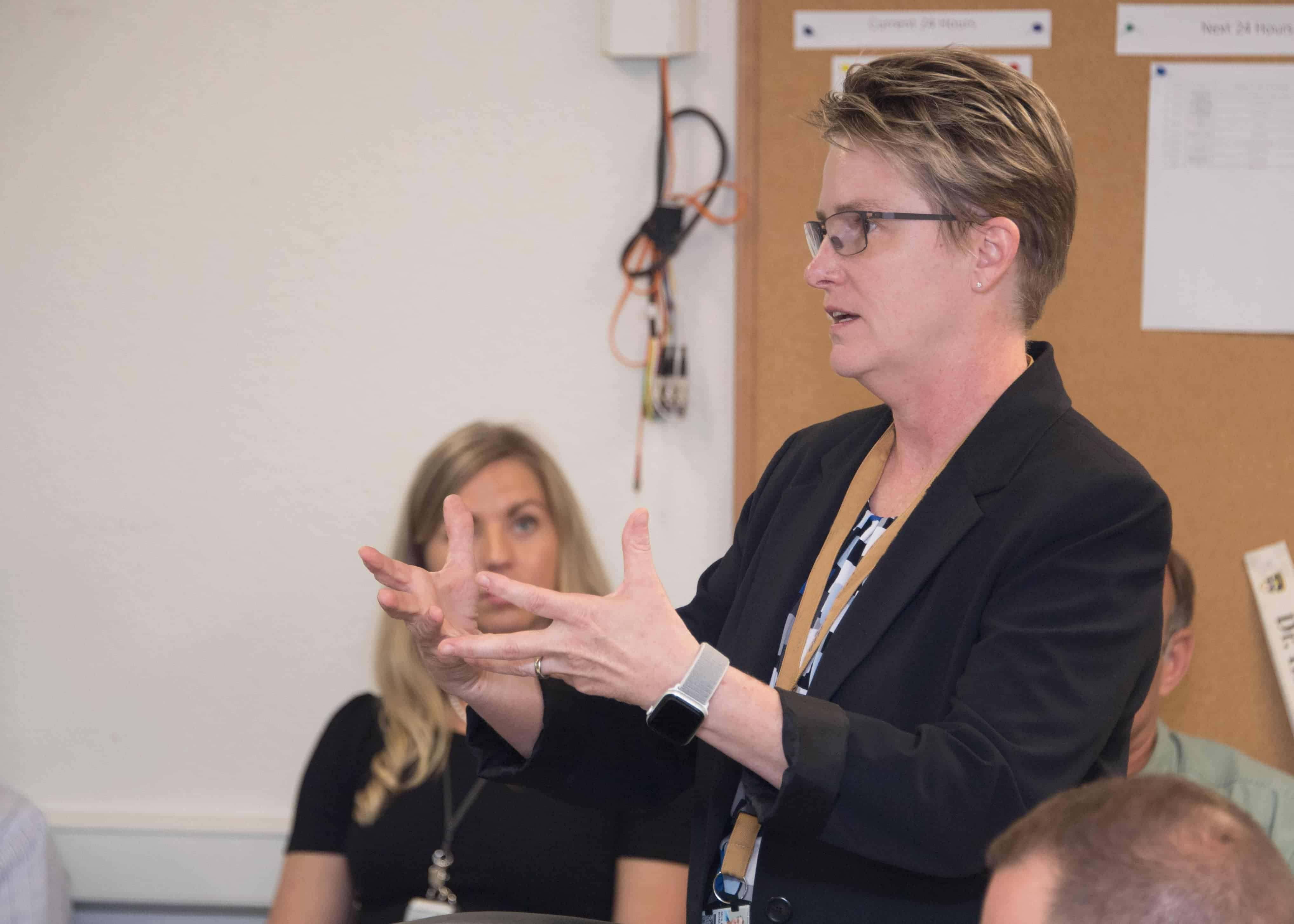 A woman presents information to a room of people. 